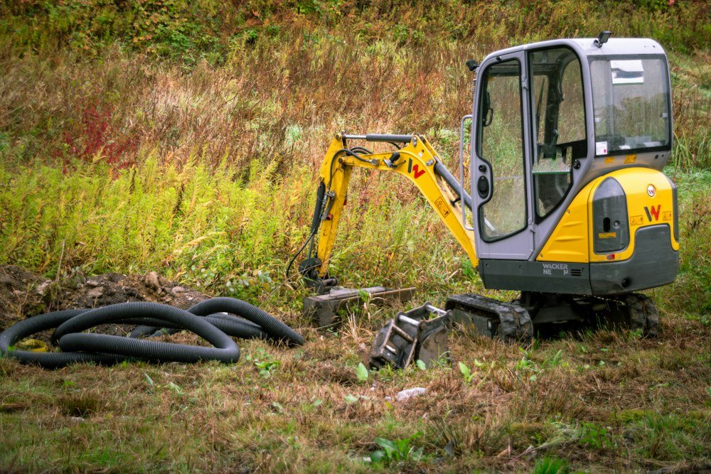 A mini excavator pulling stumps and brush on a partly cleared wooded lot